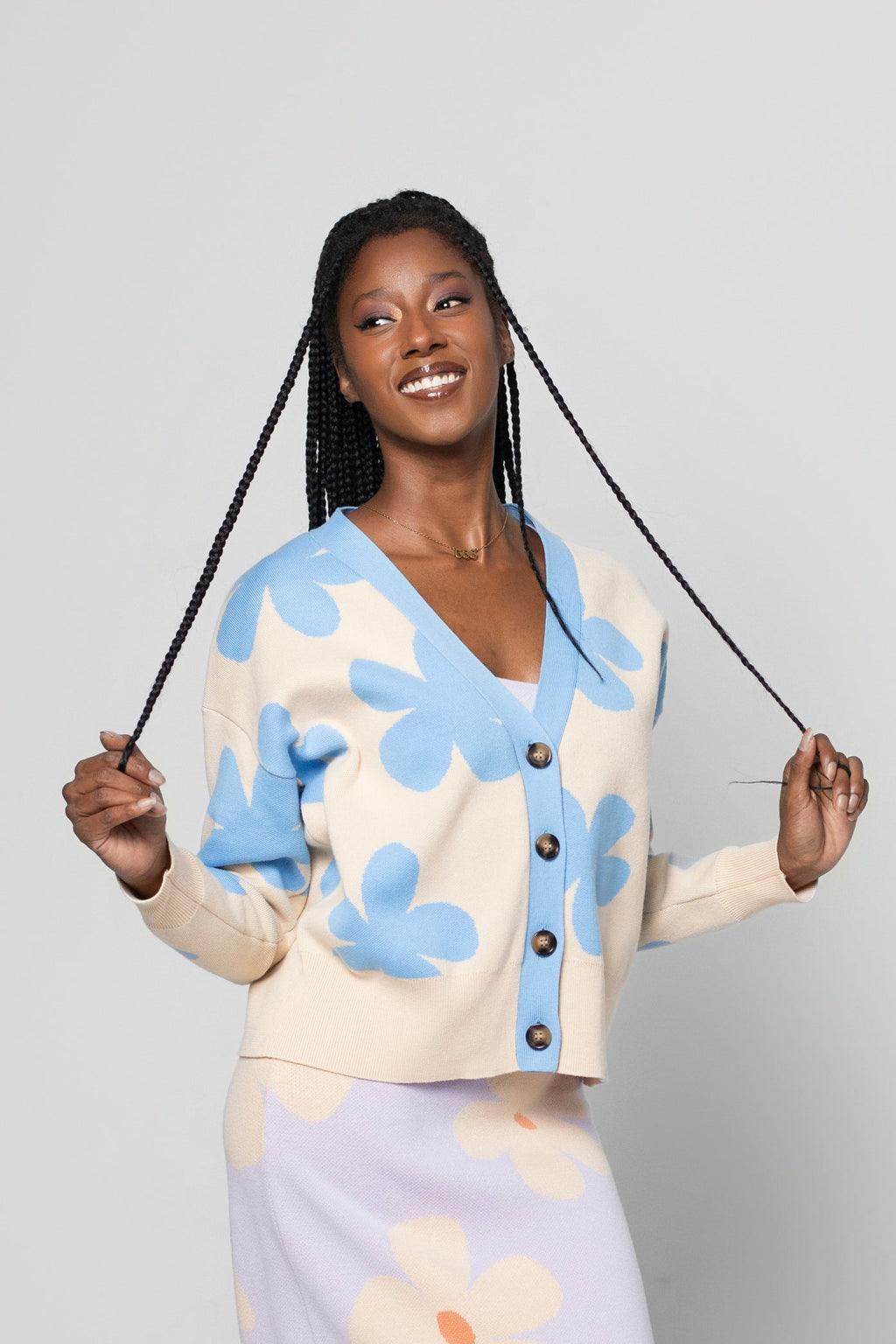A woman modeling a matching knit cardigan and midi skirt set with a floral pattern, standing against a light gray studio background.
