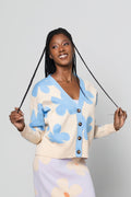 A woman modeling a matching knit cardigan and midi skirt set with a floral pattern, standing against a light gray studio background.