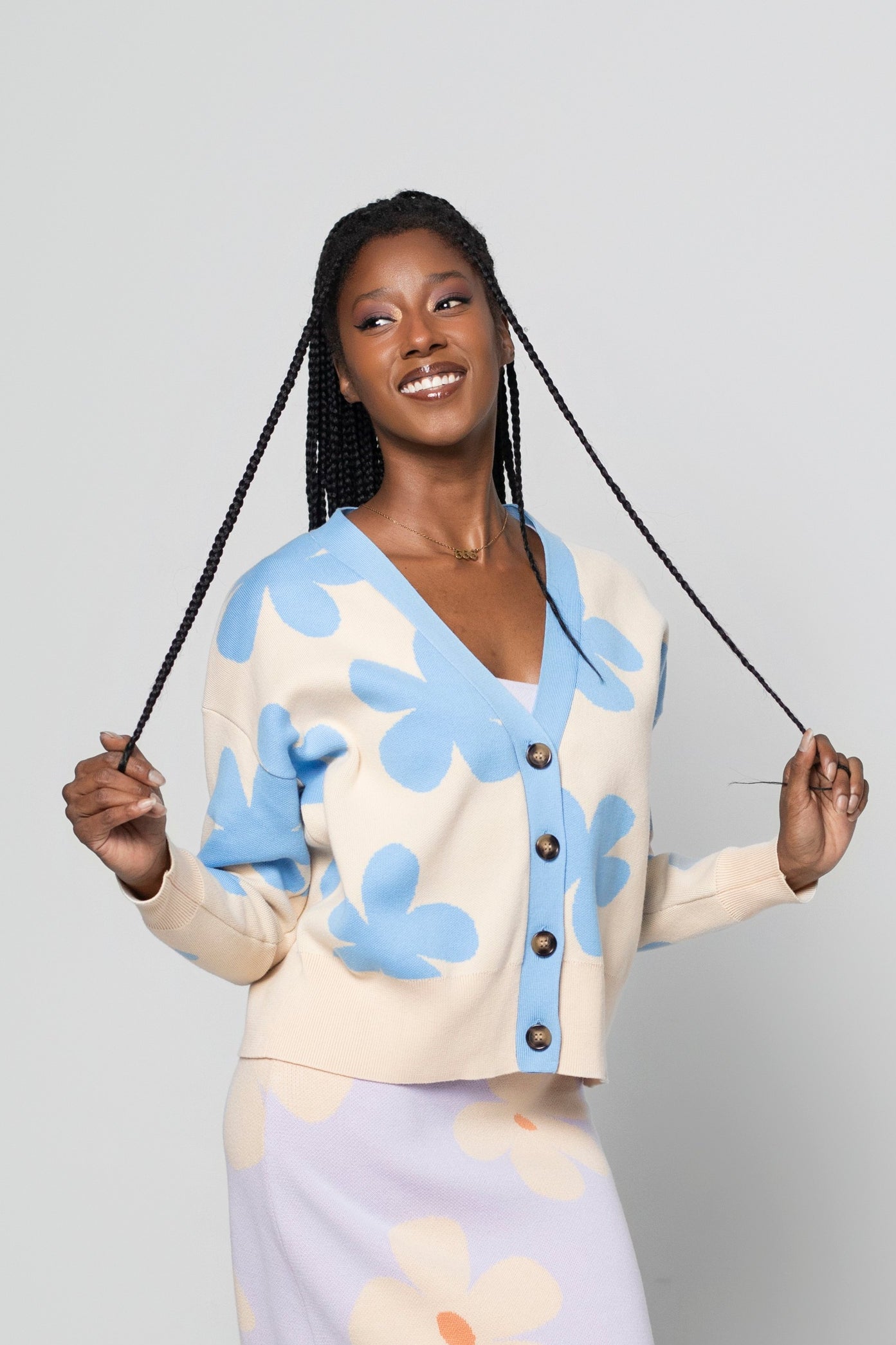 A woman modeling a matching knit cardigan and midi skirt set with a floral pattern, standing against a light gray studio background.
