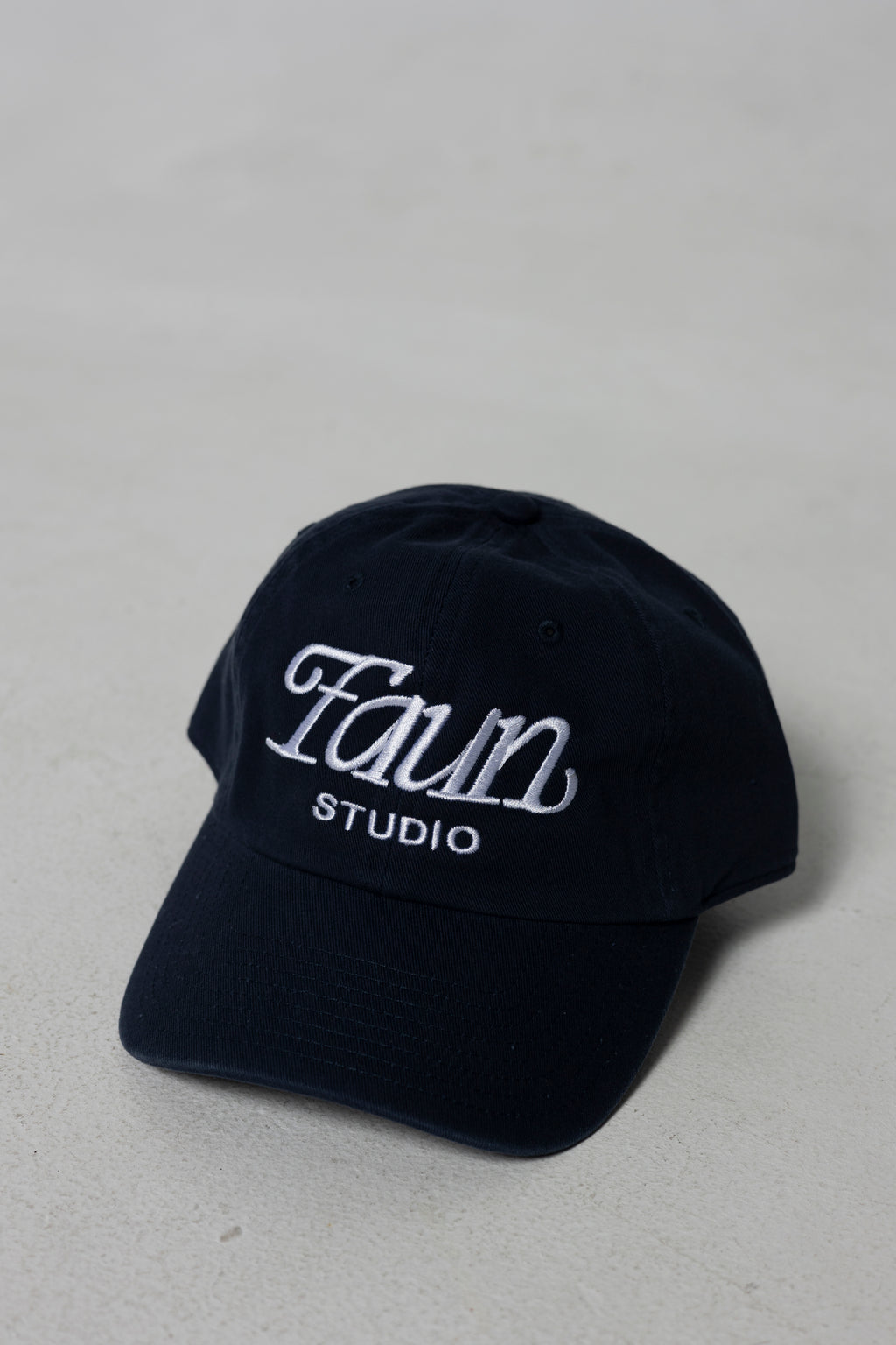 A dark navy blue baseball cap with 'Faun Studio' embroidered in white on the front, set against a neutral light gray background.