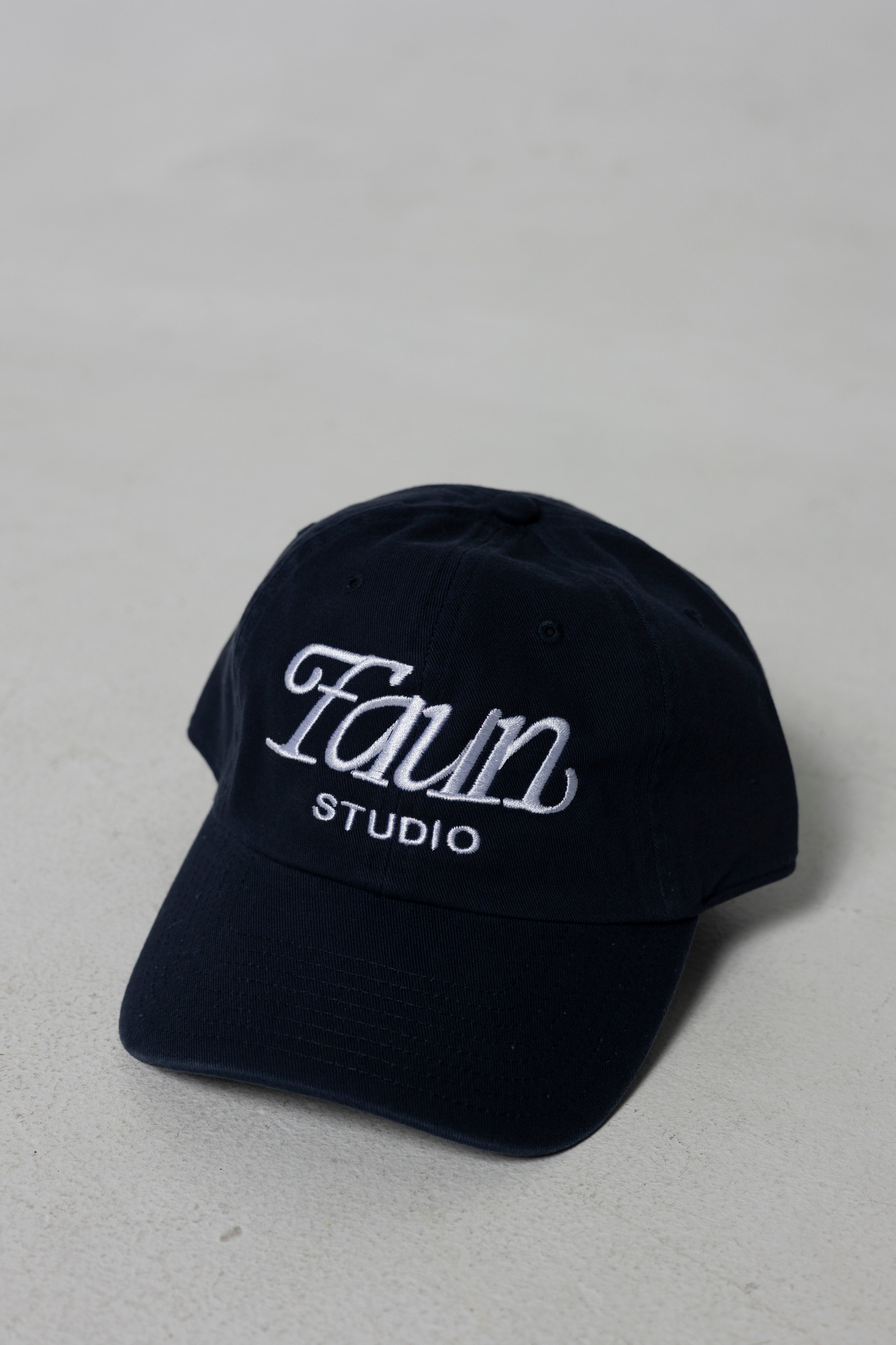 A dark navy blue baseball cap with 'Faun Studio' embroidered in white on the front, set against a neutral light gray background.