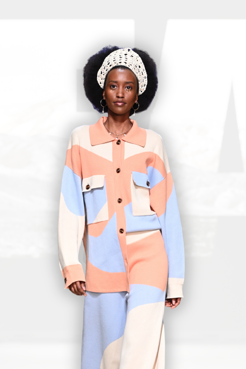 A model wearing a matching color-blocked knit set consisting of a long-sleeve button-up shirt and wide-leg trousers. The color-blocked pattern features soft pastel shades of peach, light blue, cream, and beige.