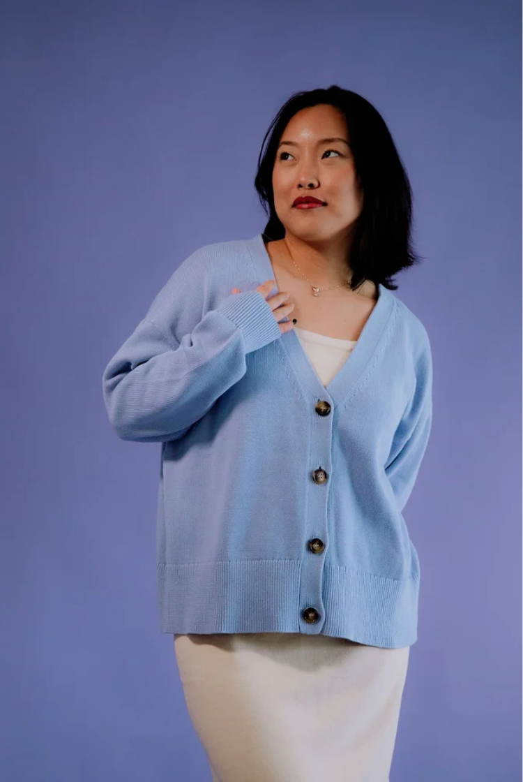 Woman wearing a light blue oversized v-neck cotton knit drop shoulder cardigan with tortoise shells. 