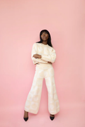 Woman wearing a tan and cream checkered shell print wide leg knit lounge pants with the matching crewneck.