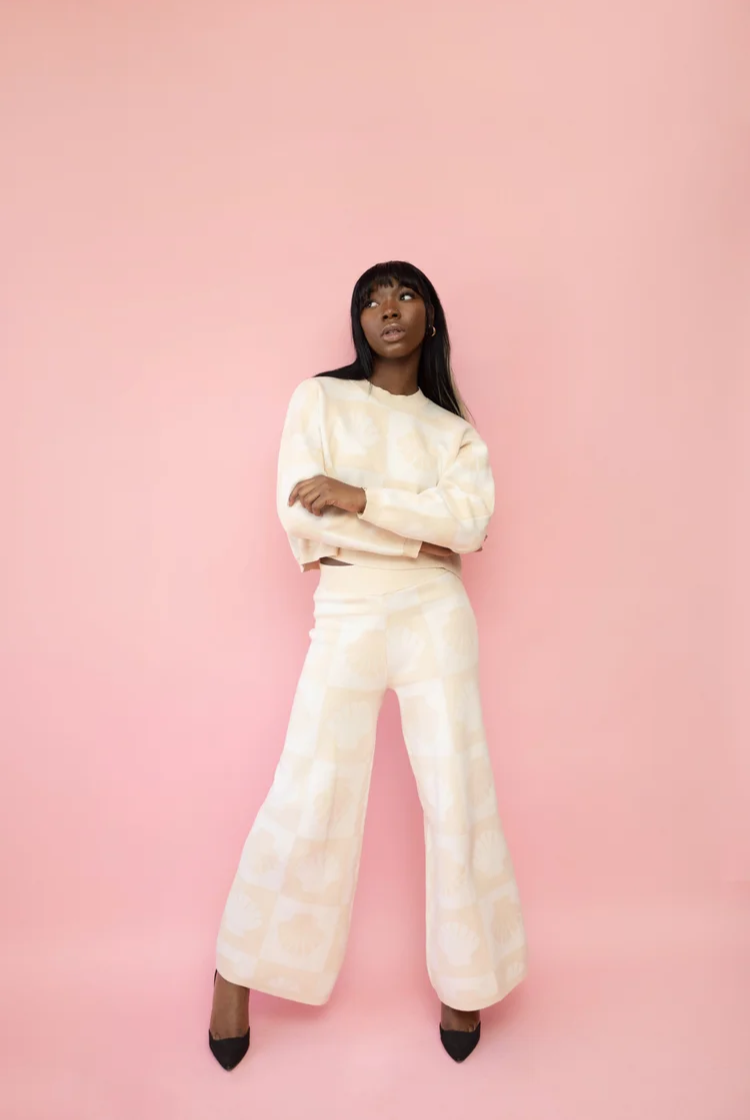 Woman wearing a tan and cream checkered shell print wide leg knit lounge pants with the matching crewneck.