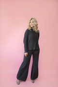 Model wearing a charcoal grey wide leg knit lounge pants with the matching ribbed cable knit polo sweater. 