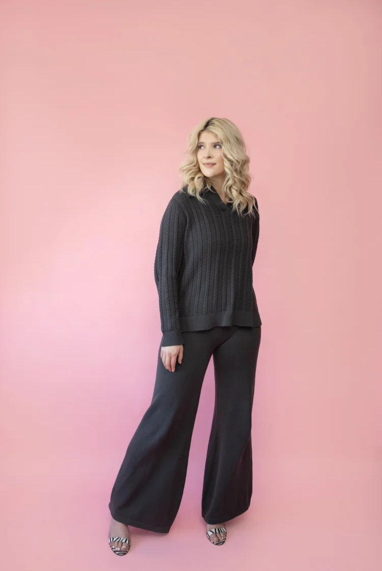 Model wearing a charcoal grey wide leg knit lounge pants with the matching ribbed cable knit polo sweater. 