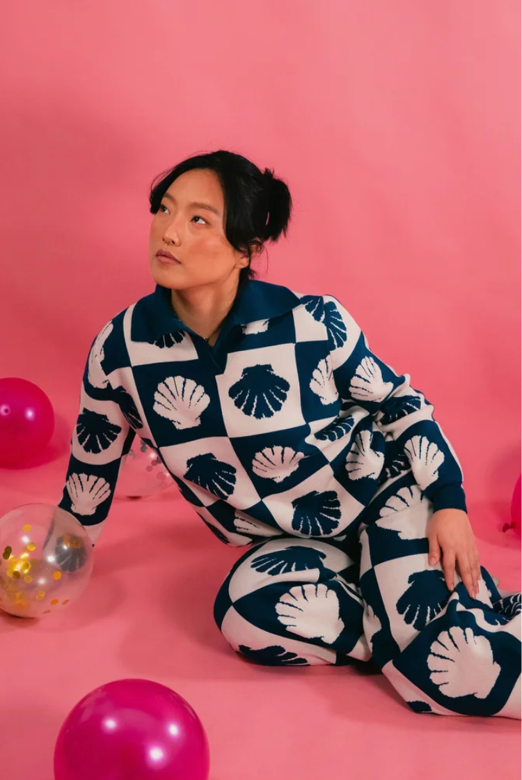 Woman wearing a blue and white, checkered and shell print knit long sleeve with polo collar. 