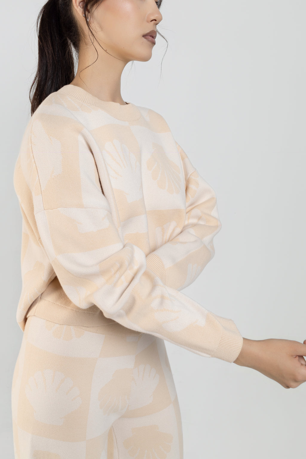 A woman wearing a beige and cream shell patterned crewneck sweatshirt and matching pants, shown from a side profile.